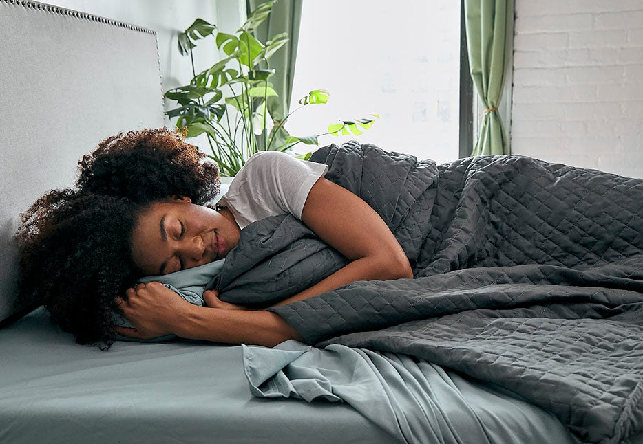 a woman sleeping under a grey weighted blanket