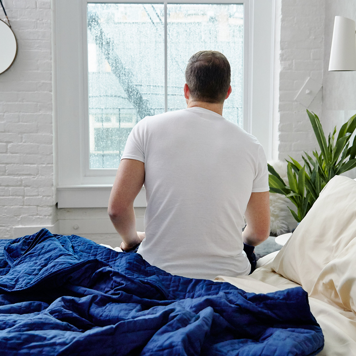 Man sitting up in bed, next to Navy Cooling Blanket