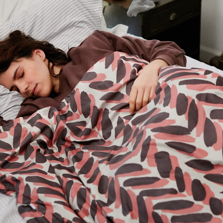 Woman sleeping in bed covered by a pink and brown weighted blanket