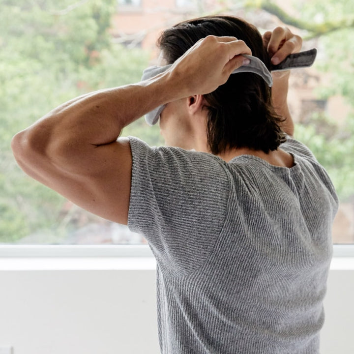 Backside of a man's head as he's putting on a grey weighted eye mask