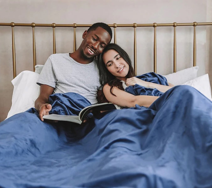a couple reading a book together in bed under a blue weighted blanket