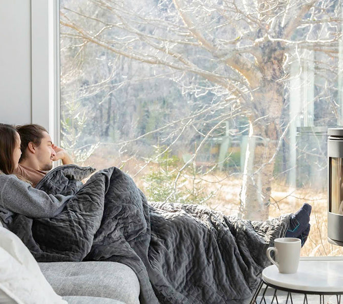 a couple sitting together on a couch under a weighted blanket