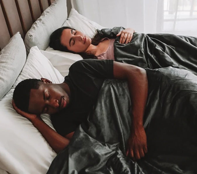 a couple sleeping under a grey weighted blanket