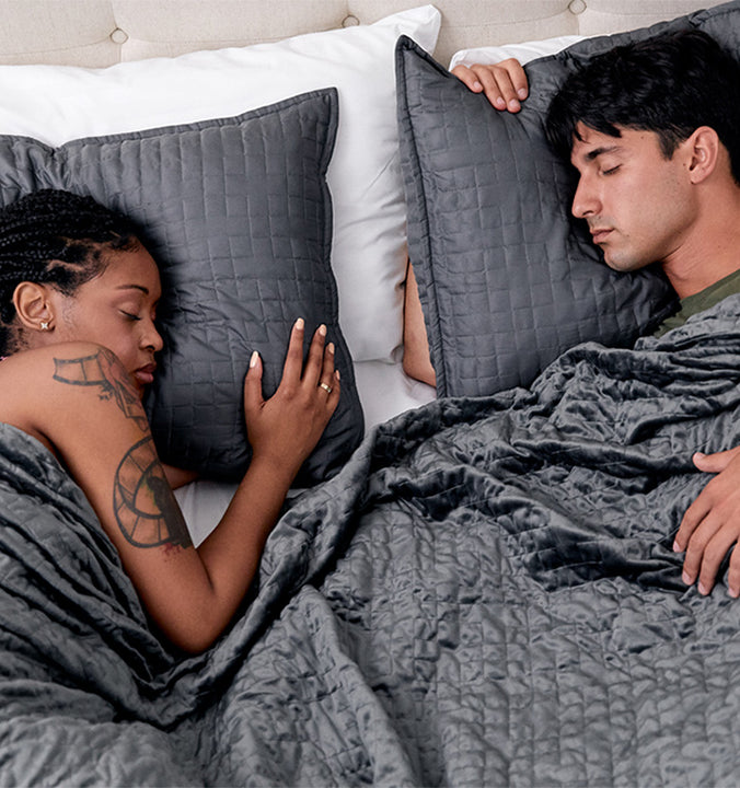 a couple sleeping under a grey weighted blanket