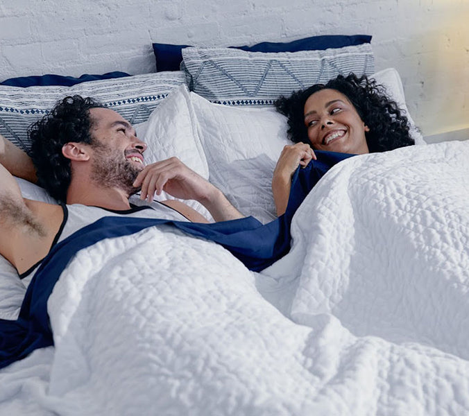 a couple talking while laying under a white weighted blanket