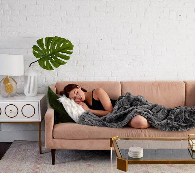 a woman sleeping on a couch under a gray weighted blanket