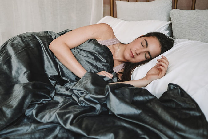 a woman sleeping under a gray weighted blanket