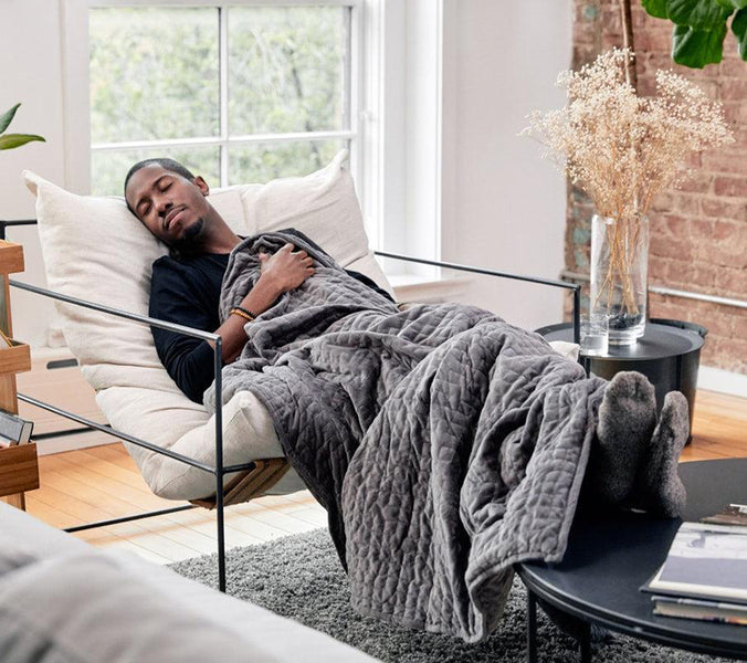 a man sleeping in a lounge chair under a weighted blanket