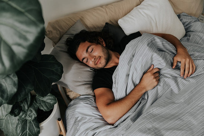a man sleeping under a gray pinstripe weighted blanket