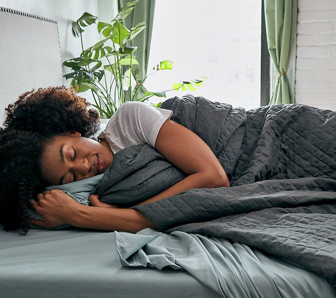 a woman sleeping under a grey weighted blanket